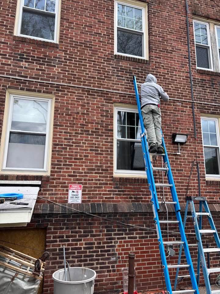 Electrician on a ladder installing outdoor lighting on a brick building