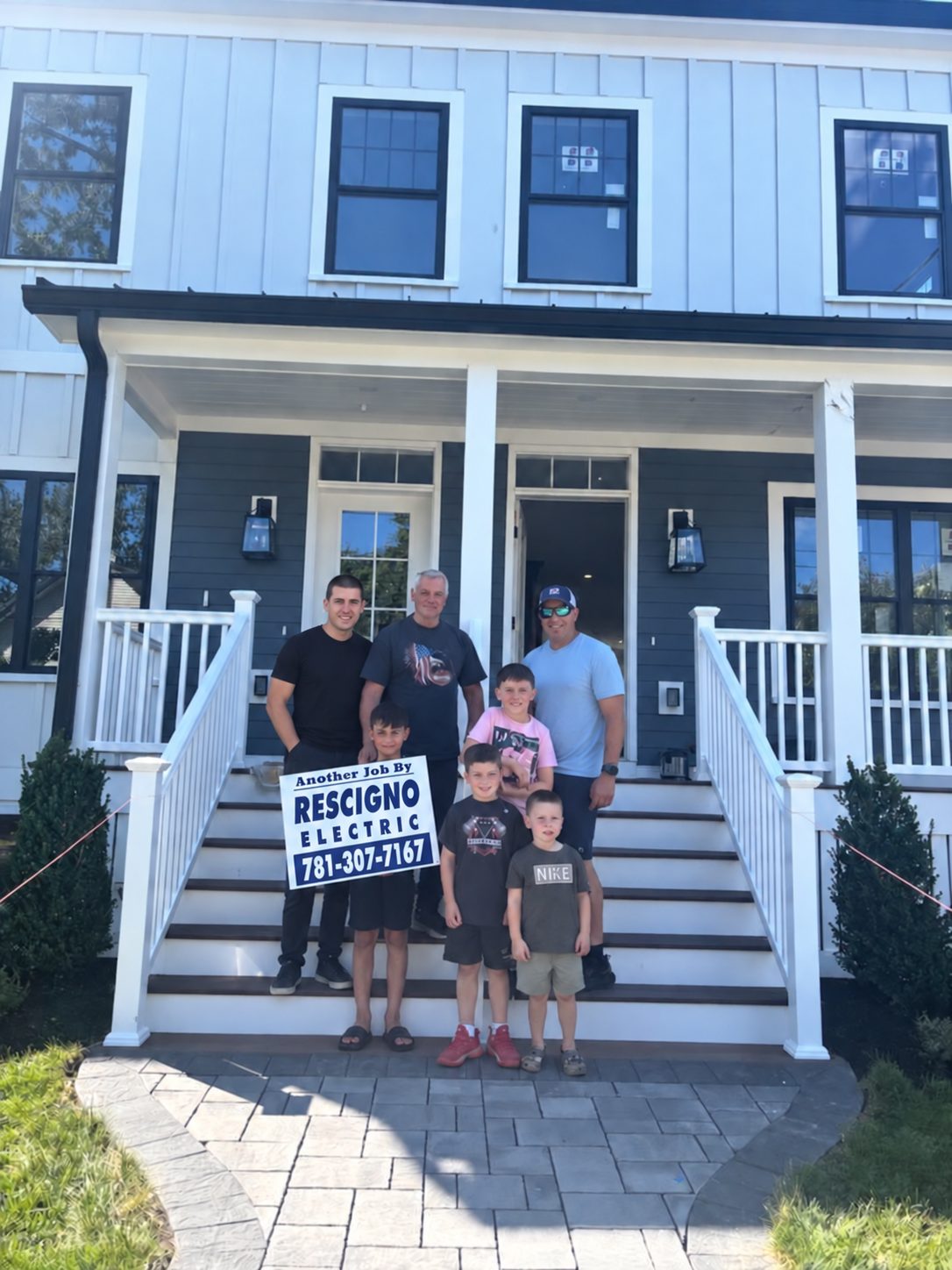Three generations of the Rescigno family standing on the front steps of a home they wired, holding an Another Job By Rescigno Electric sign